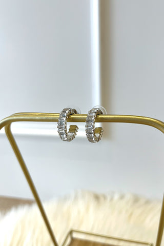 Silver hoop earrings on a gold stand against a white background