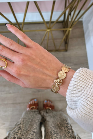 Hand wearing a gold bracelet with a blurred background