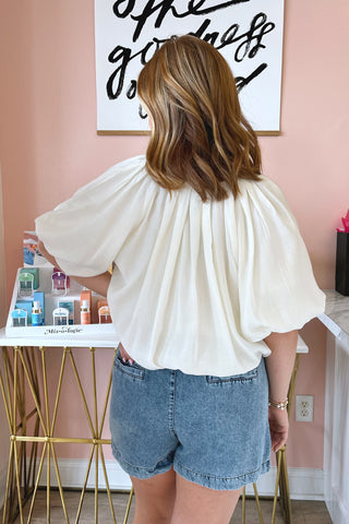 The back of an ivory colored oversized balloon blouse with dramatic pleats along the neckline. 