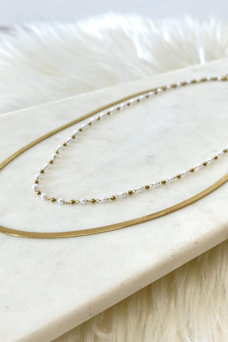 Two gold necklaces on a white marble surface