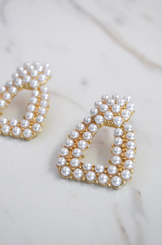 Pearl and gold teardrop-shaped earrings on a marble surface
