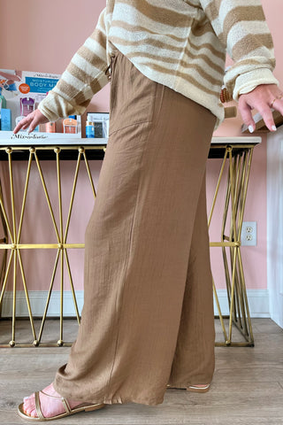 Person wearing a beige and white striped sweater and brown wide-leg pants in a room with a pink wall and gold legs.