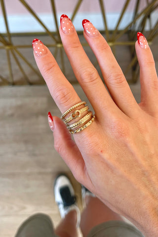 Hand with red nail polish wearing multiple gold rings, blurred background