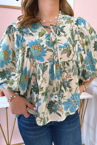 Person wearing a floral blouse with blue and green patterns against a pink background