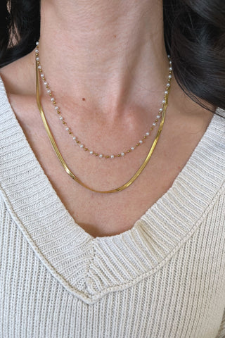 Close-up of a person wearing two necklaces with a light-colored sweater.