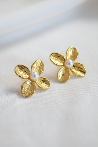 Gold flower-shaped earrings with pearl centers on a light background
