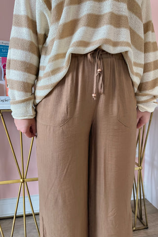 Person wearing a striped sweater and brown wide-leg pants in a minimal indoor setting.