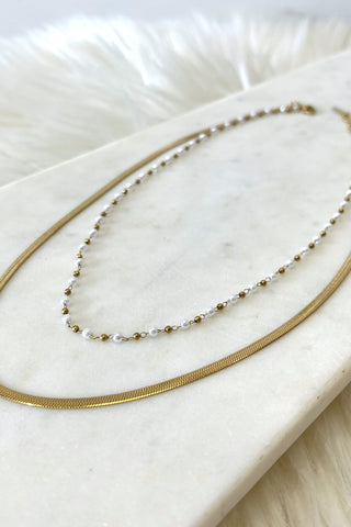 Two necklaces on a marble surface, one gold and one with pearls.