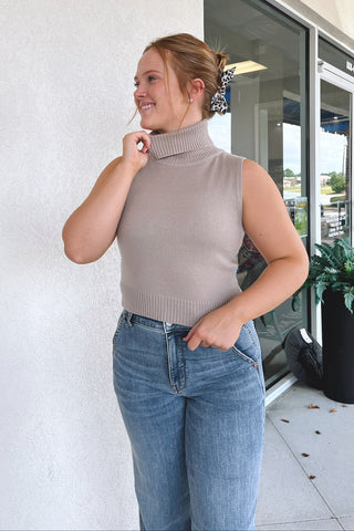 Model wearing beige turtle neck sweater in front of white wall.