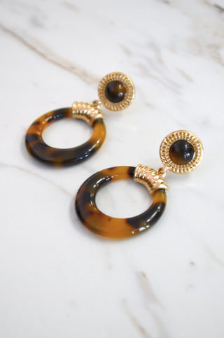 Tortoiseshell hoop earrings with gold accents on a marble background