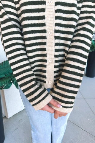 A person wearing a green and cream striped knit cardigan with a cream ribbed button placket and cuffs, paired with light blue jeans.