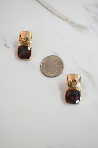 Pair of gold and tortoiseshell square earrings on a white surface with a coin for scale.