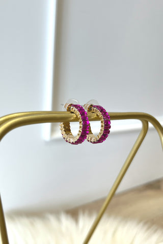 Gold hoop earrings with pink gemstones on a gold stand against a white background