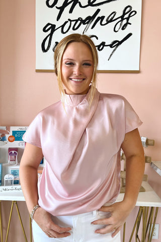 Woman wearing a pink blouse standing in a room with a painting on the wall.