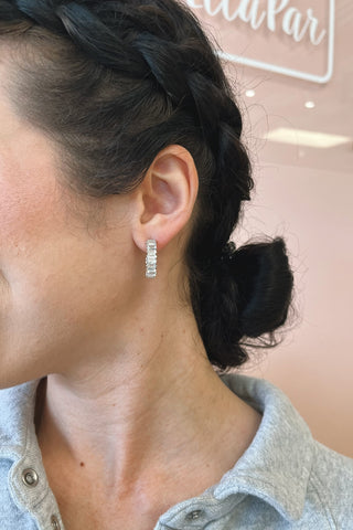 Close-up of a person wearing diamond hoop earrings with a blurred background