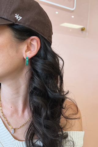 Close-up of a person wearing green earrings with a blurred background