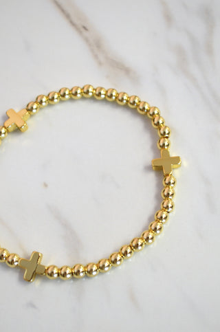 Gold beaded bracelet with cross charms on a marble surface