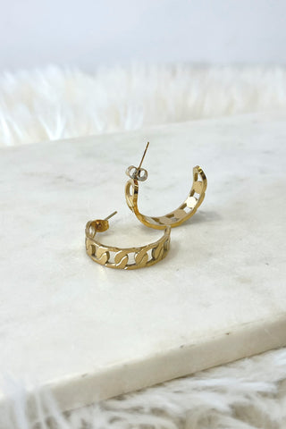 Gold hoop earrings on a white marble surface with a soft white background