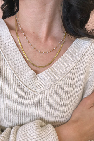 Close-up of a person wearing a beige sweater and layered necklaces.
