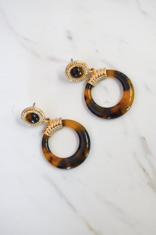 Tortoiseshell hoop earrings with gold accents on a white marble surface