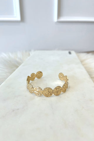 Gold bracelet on a white marble surface with a light gray background