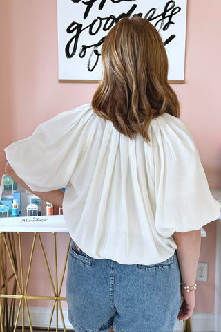 The back of an ivory colored oversized balloon blouse with dramatic pleats along the neckline. 