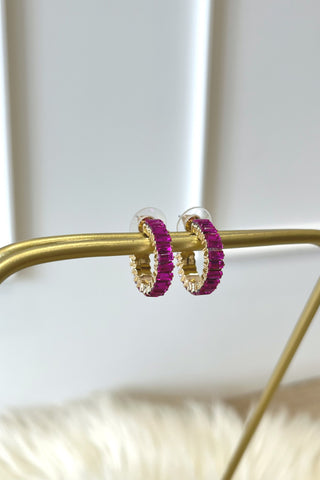 Gold hoop earrings with pink gemstones on a gold stand against a white background