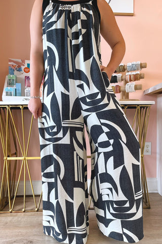 Person wearing a black and white patterned jumpsuit in a room with a pink wall.