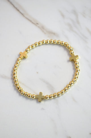 Gold bracelet with cross charms on a marble surface