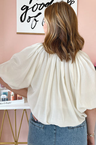 The back of an ivory colored oversized balloon blouse with dramatic pleats along the neckline. 