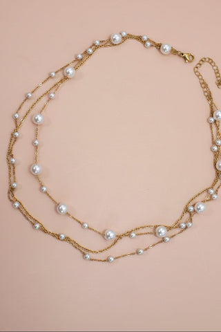 Three-layered pearl necklace on a pink background
