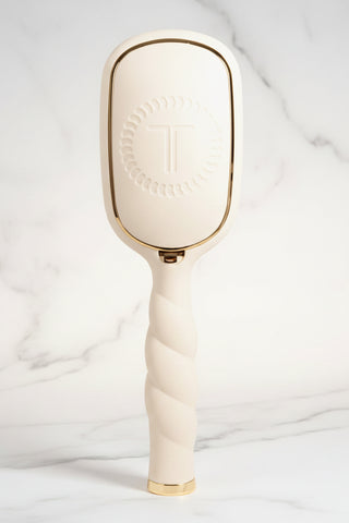 Cream-colored paddle hairbrush with gold accents on a white background